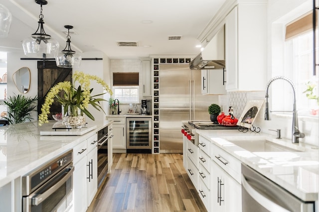 kitchen featuring wood-type flooring, white cabinetry, appliances with stainless steel finishes, exhaust hood, and beverage cooler