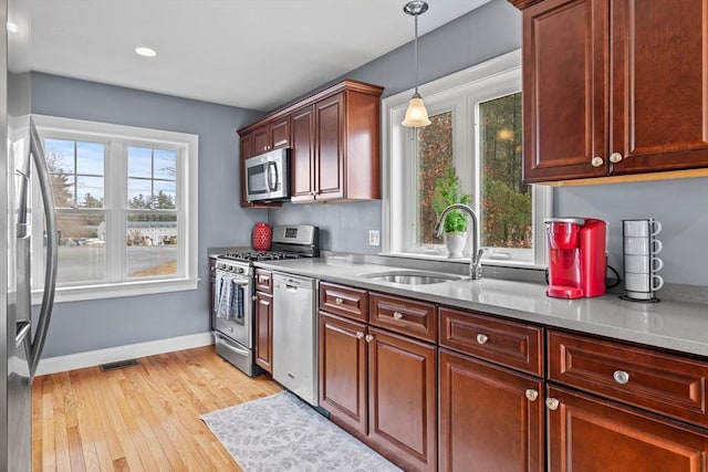 kitchen with visible vents, light wood-style flooring, appliances with stainless steel finishes, hanging light fixtures, and a sink