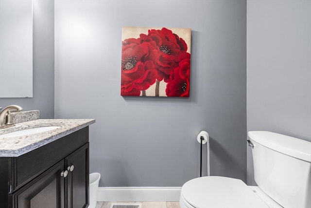 half bath with vanity, toilet, visible vents, and baseboards