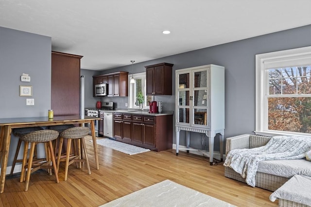 kitchen featuring a sink, stainless steel appliances, light countertops, dark brown cabinets, and light wood-style floors