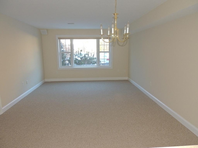 carpeted spare room featuring an inviting chandelier