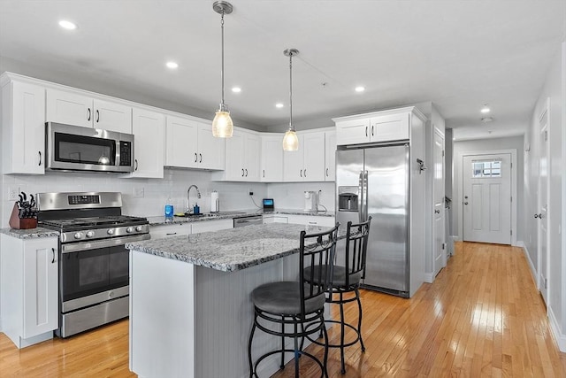 kitchen with stainless steel appliances, decorative light fixtures, light hardwood / wood-style flooring, a center island, and white cabinetry