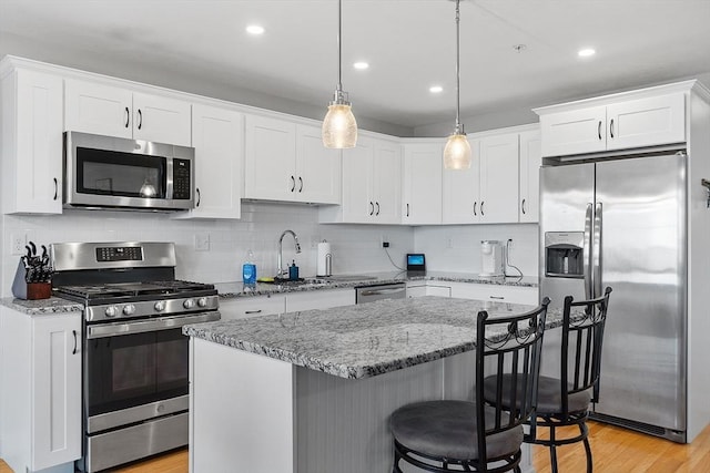 kitchen with white cabinetry, light stone countertops, light hardwood / wood-style flooring, pendant lighting, and appliances with stainless steel finishes