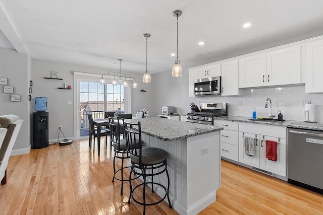 kitchen with hanging light fixtures, sink, appliances with stainless steel finishes, a kitchen island, and white cabinetry