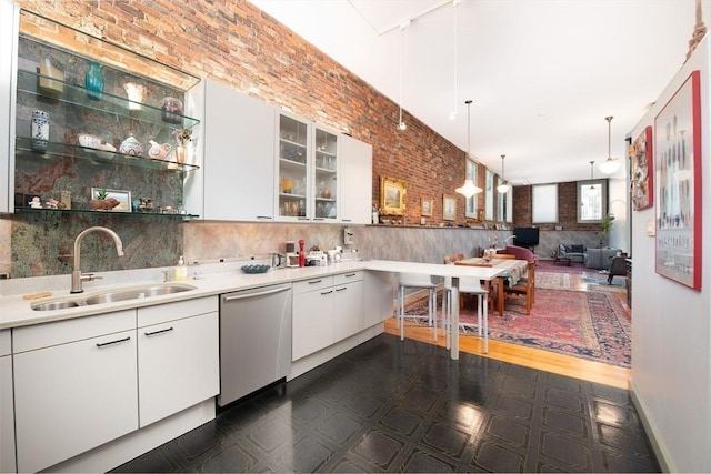 kitchen featuring pendant lighting, sink, dishwasher, white cabinets, and brick wall