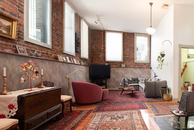 living area with hardwood / wood-style floors, a towering ceiling, and brick wall