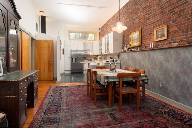 dining area featuring hardwood / wood-style floors, brick wall, and a high ceiling