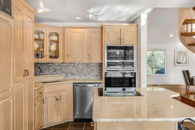 kitchen featuring stainless steel appliances, a center island, a sink, light stone counters, and light brown cabinets