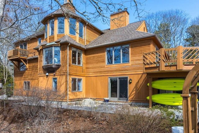 back of property featuring a wooden deck, roof with shingles, and a chimney