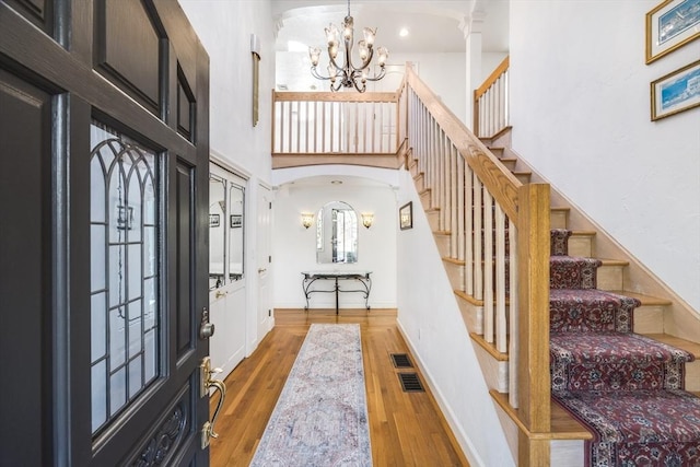 foyer featuring stairway, a high ceiling, an inviting chandelier, arched walkways, and hardwood / wood-style flooring