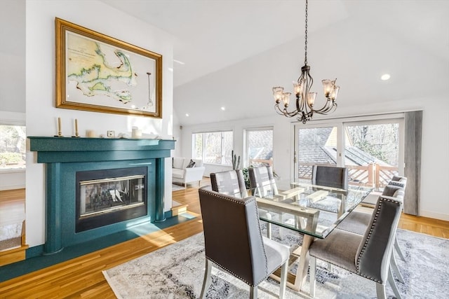 dining room with lofted ceiling, a wealth of natural light, a chandelier, and a fireplace with flush hearth