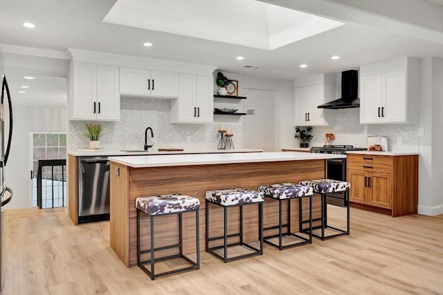 kitchen featuring a center island, stainless steel appliances, light hardwood / wood-style floors, and wall chimney range hood