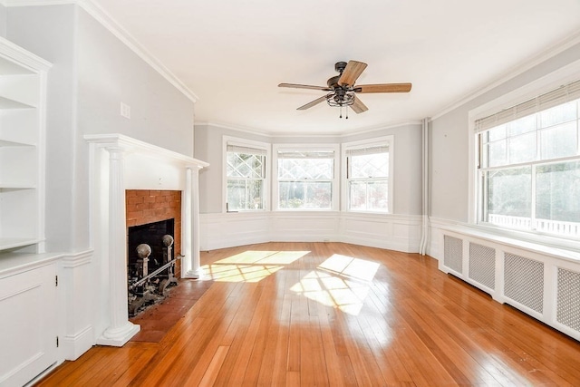 unfurnished living room with ornate columns, radiator, crown molding, light wood-type flooring, and a fireplace