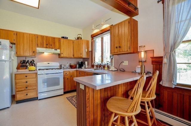 kitchen with white appliances, sink, a baseboard heating unit, kitchen peninsula, and a breakfast bar area