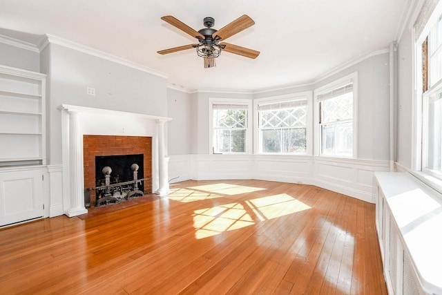 unfurnished living room featuring ceiling fan, ornamental molding, a fireplace, built in shelves, and light hardwood / wood-style floors