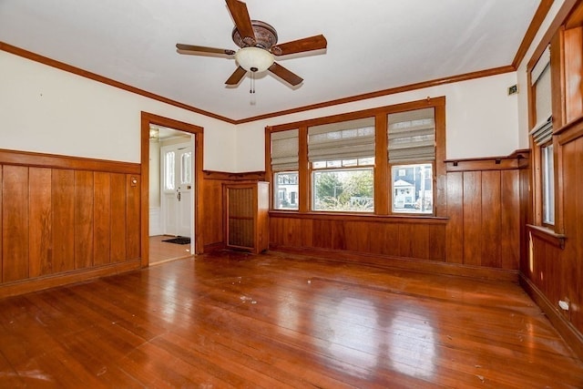 spare room with hardwood / wood-style floors, crown molding, wooden walls, and ceiling fan