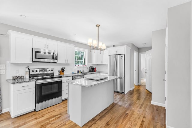 kitchen with white cabinets, stainless steel appliances, a center island, and light hardwood / wood-style flooring