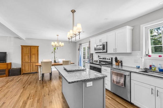 kitchen featuring light hardwood / wood-style floors, hanging light fixtures, a kitchen island, white cabinetry, and appliances with stainless steel finishes