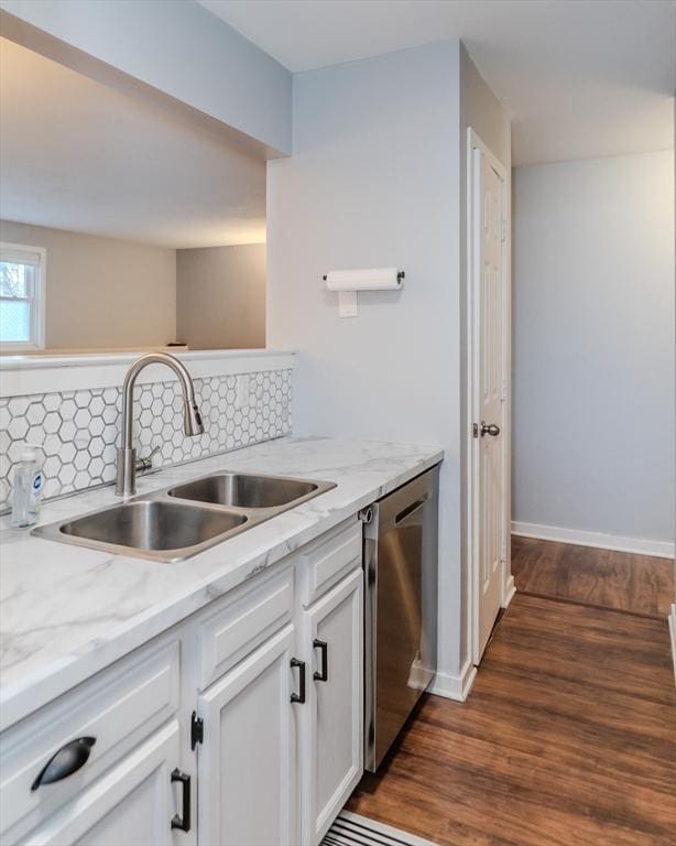 kitchen with a sink, white cabinets, stainless steel dishwasher, dark wood-style floors, and tasteful backsplash