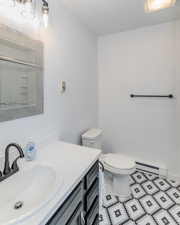 full bath with a shower, toilet, a baseboard heating unit, vanity, and baseboards