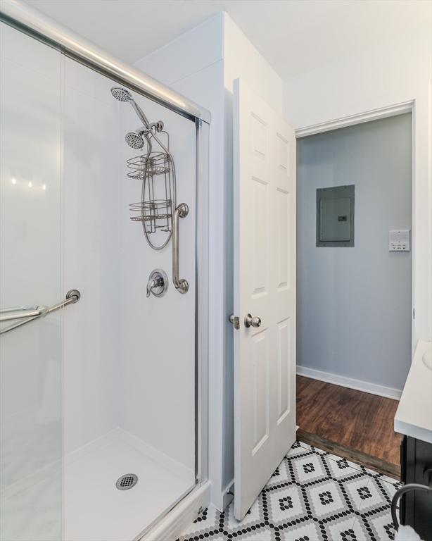 bathroom with a shower stall, electric panel, baseboards, and wood finished floors