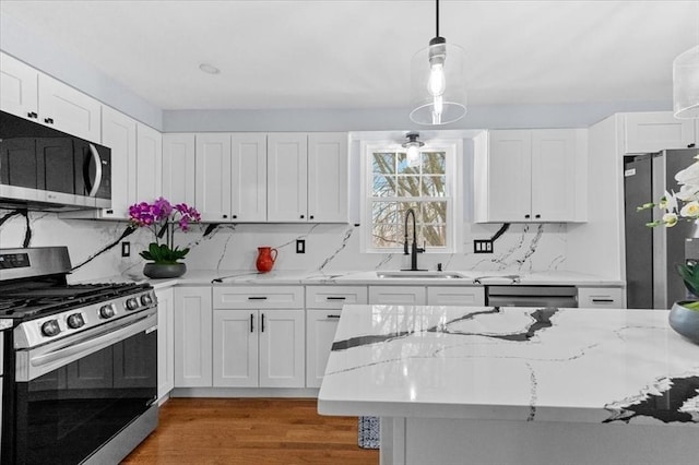 kitchen with sink, hanging light fixtures, light stone countertops, appliances with stainless steel finishes, and white cabinetry