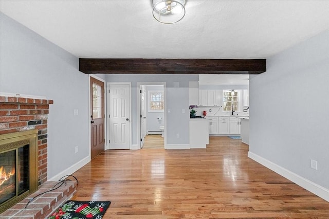 unfurnished living room featuring beam ceiling, light wood-type flooring, a fireplace, and a baseboard heating unit