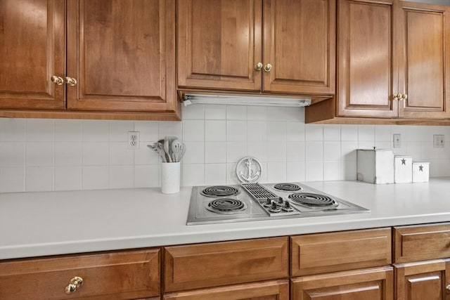 kitchen with stainless steel electric cooktop, light countertops, brown cabinetry, and tasteful backsplash