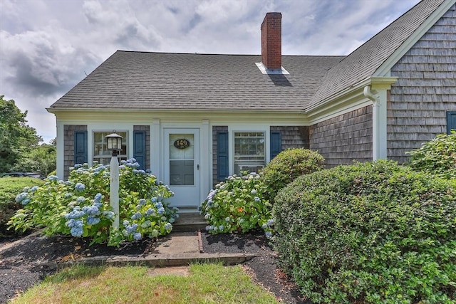 entrance to property with a chimney and a shingled roof