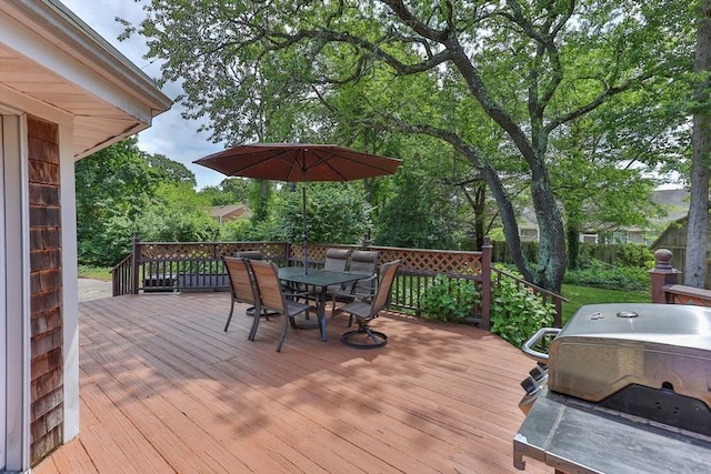 deck with outdoor dining space, a grill, and view of wooded area