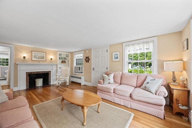 living room featuring radiator heating unit, wood finished floors, a fireplace, and baseboards