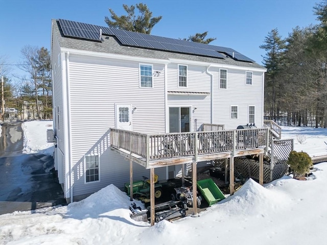 snow covered back of property with roof mounted solar panels and a deck