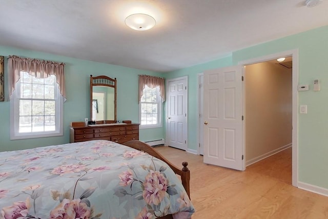 bedroom with a baseboard heating unit, light wood-style flooring, and baseboards