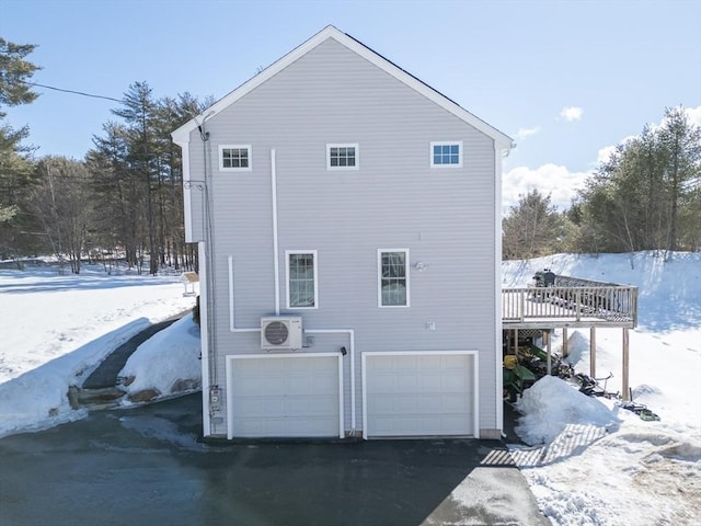 snow covered property with a garage, driveway, a deck, and ac unit