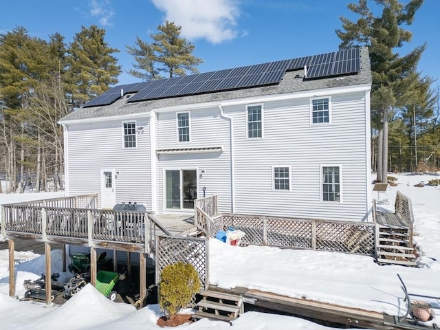 snow covered property with a shingled roof, stairway, a deck, and solar panels