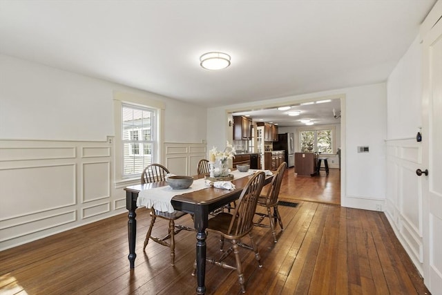 dining room featuring visible vents, dark wood-style flooring, a decorative wall, and a wainscoted wall