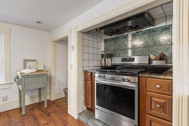 kitchen featuring brown cabinets, stainless steel gas stove, dark wood finished floors, tasteful backsplash, and under cabinet range hood