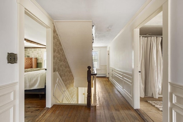 corridor with a decorative wall, wallpapered walls, hardwood / wood-style flooring, and a wainscoted wall