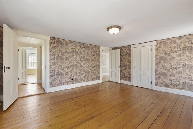 empty room with wallpapered walls, baseboards, and hardwood / wood-style floors