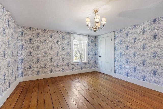 empty room with wood-type flooring, wallpapered walls, a notable chandelier, and baseboards