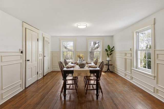 dining area featuring wainscoting, a decorative wall, and dark wood-style floors