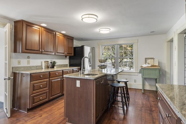 kitchen featuring a sink, dark wood-style flooring, freestanding refrigerator, and a breakfast bar