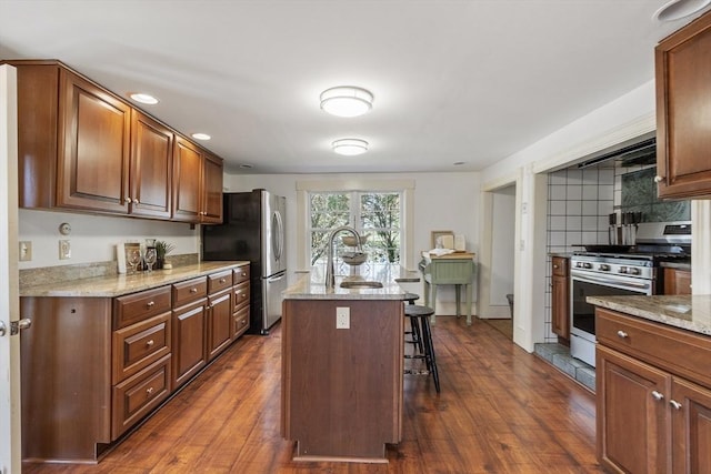 kitchen with a sink, appliances with stainless steel finishes, a kitchen bar, and dark wood finished floors
