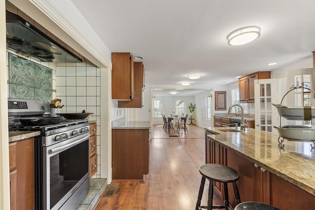 kitchen featuring brown cabinets, a sink, stainless steel range with gas cooktop, a kitchen bar, and dark wood-style floors