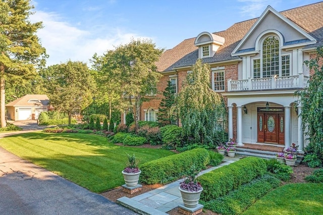 view of front of house featuring brick siding, a balcony, a front lawn, and roof with shingles