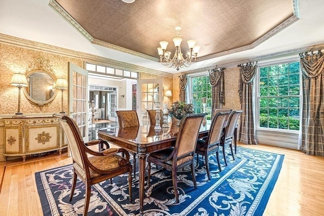 dining room featuring wallpapered walls, a raised ceiling, light wood-style flooring, ornamental molding, and an inviting chandelier