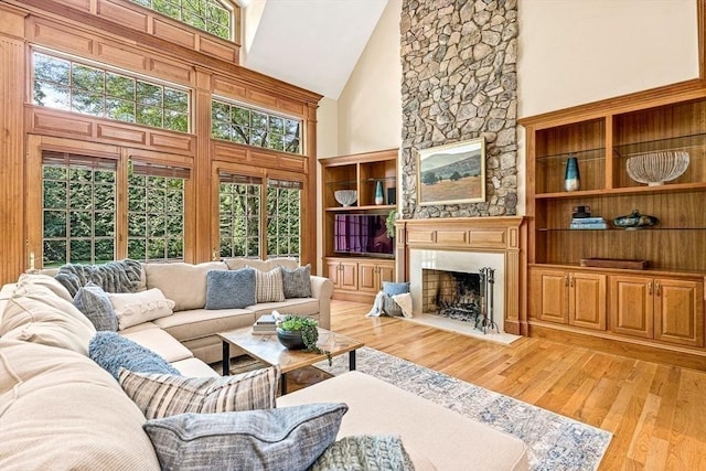 living room with high vaulted ceiling, light wood finished floors, a fireplace with flush hearth, and built in shelves