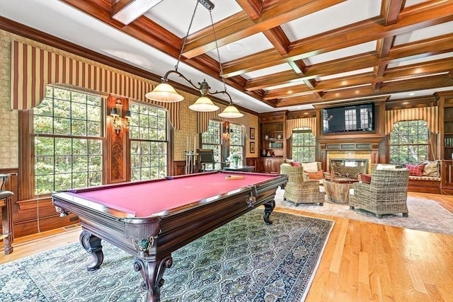 playroom featuring coffered ceiling, wood finished floors, beamed ceiling, a glass covered fireplace, and crown molding