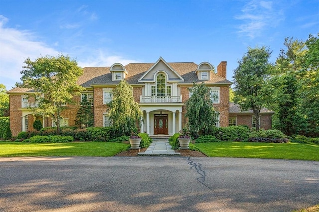 colonial house with brick siding, a chimney, a front yard, and a balcony