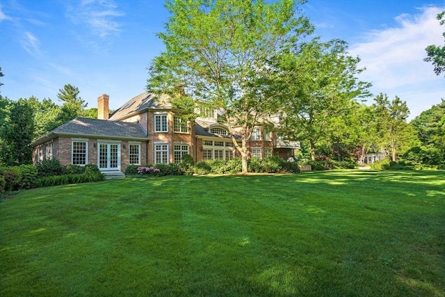 back of house with a yard, french doors, a chimney, and an attached garage